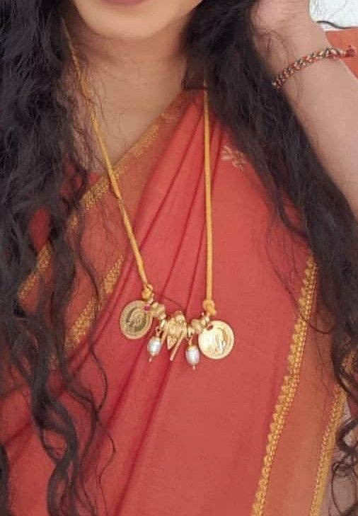 a woman with long black hair wearing a red sari and gold necklace on her neck