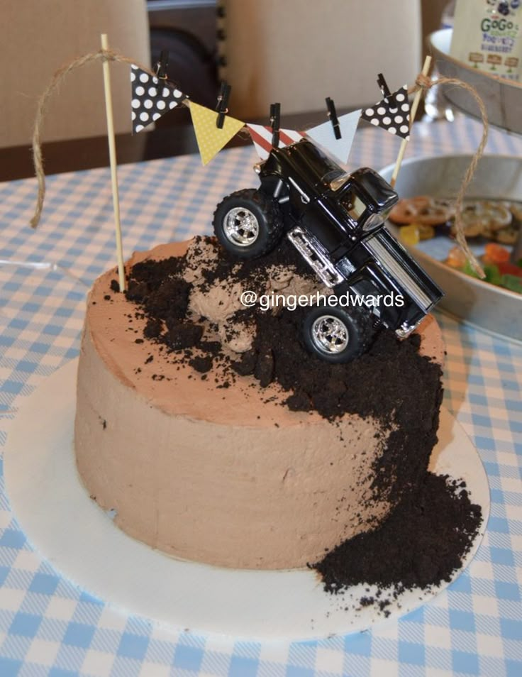 a birthday cake with a car on top and dirt in the middle, sitting on a blue checkered tablecloth