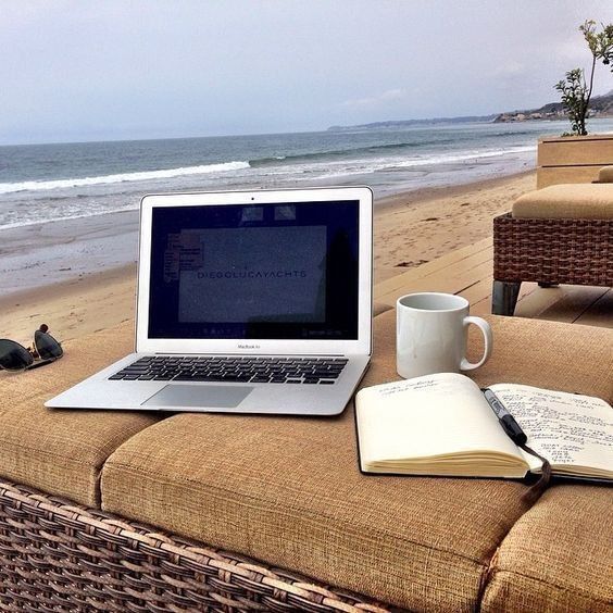 an open laptop computer sitting on top of a table next to a book and cup