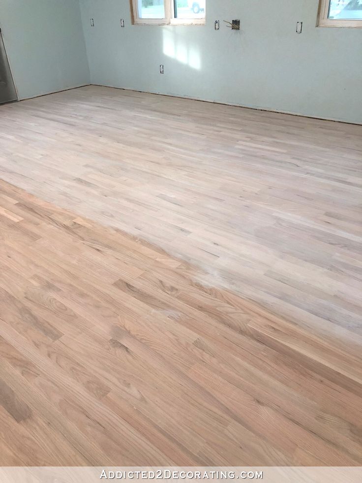 an empty room with hard wood flooring in the foreground and windows on the far wall