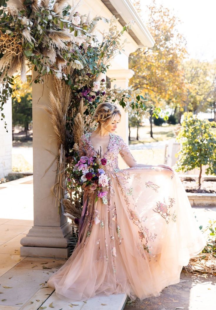 a woman in a pink dress is sitting on a bench with flowers and greenery