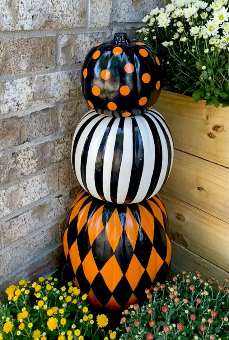 three black and white pumpkins sitting on top of each other in front of flowers