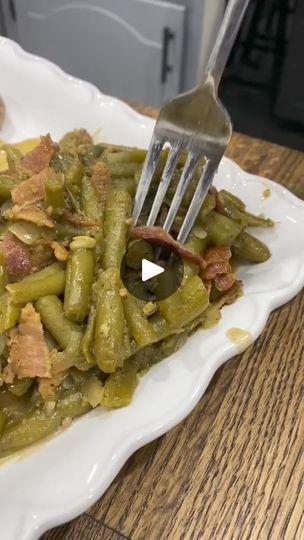 a white plate topped with green beans covered in bacon next to a knife and fork