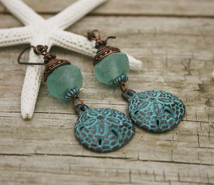 MYKONOS GREEN PATINA SAND DOLLAR AND AQUA AFRICAN GLASS EARRINGS Greek Sand Dollar charms dangle beneath African glass beads in aquamarine.  A shell shaped copper bead cap tops the glass. Sensitive ears? Hypoallergenic niobium earwires in antique brass with a copper ball. Great gift for your favorite beach lover!  2 1/2 inches View more She Shellz Earrings here: https://www.etsy.com/shop/SheShellzByCaptDeb?ref=seller-platform-mcnav&section_id=14171400 Thanks for cruising with Captain Deb! Turquoise Wire Wrapped Earrings For Beach, Handmade Beachy Green Jewelry, Green Beachy Jewelry For Beach Season, Bohemian Green Jewelry For Beach Season, Beachy Green Jewelry For Beach Season, Green Jewelry With Matching Earrings For The Beach, Nickel-free Green Earrings For Beach, Sand Dollar Earrings, Tropical Earrings