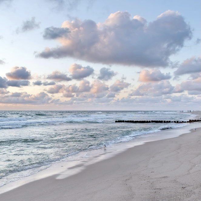 a beach with waves crashing on the shore and clouds in the sky over the water