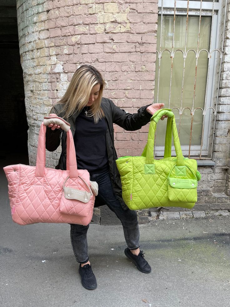 a woman holding two purses in front of a brick building