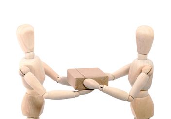 two wooden mannequins are playing with a small box on the floor,