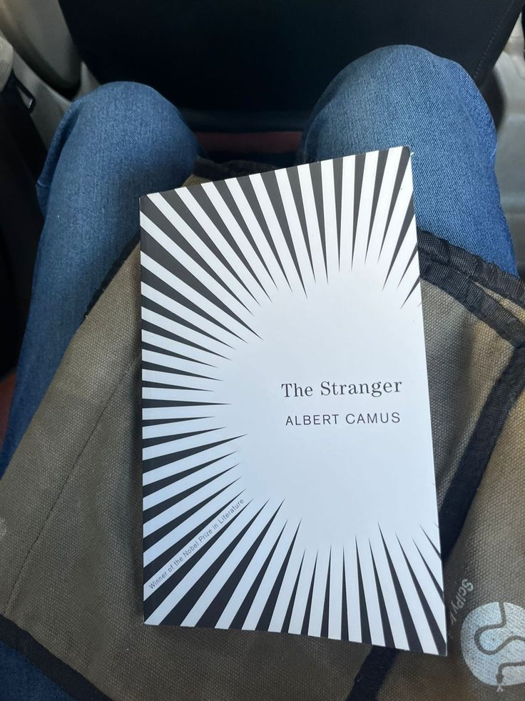 the strange albert camus book is sitting on someone's lap in their car seat