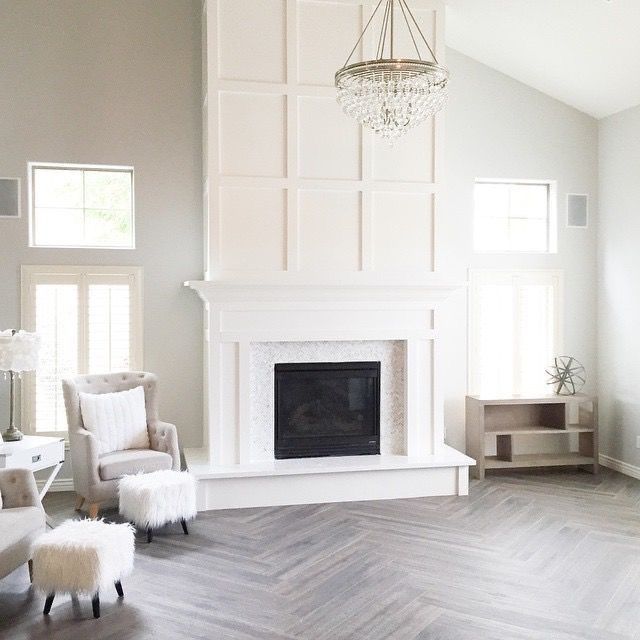 a living room with white furniture and a chandelier hanging from the ceiling over a fireplace