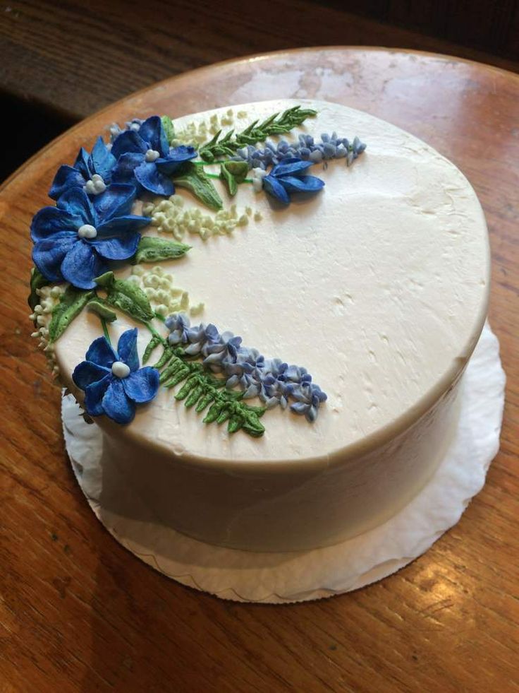 a white cake with blue flowers on it sitting on top of a wooden table next to a knife