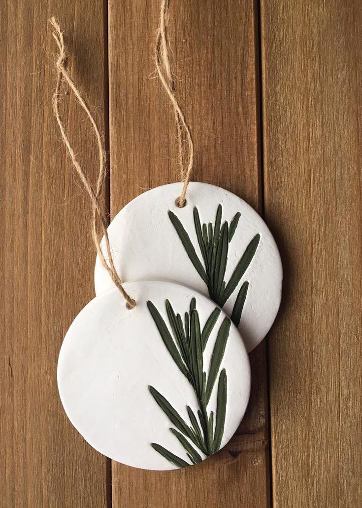 two white ceramic ornaments with green leaves hanging from twine on wooden surface, closeup