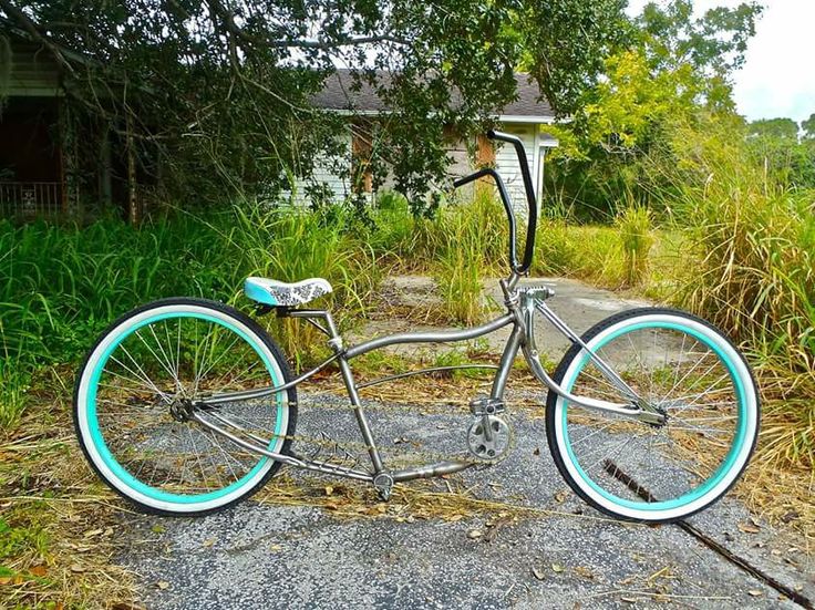 an old bicycle is sitting on the ground in front of some grass and bushes with a house in the background