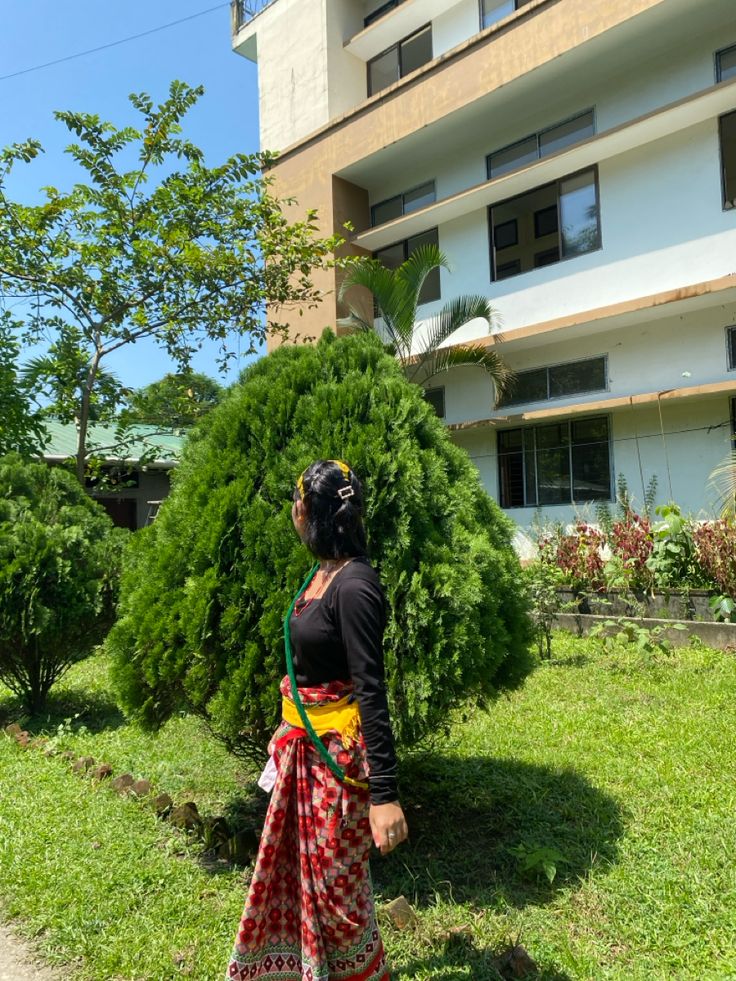 a woman standing in front of a tall building next to a lush green field with trees