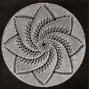 a white doily with an intricate design in the shape of a flower on black paper