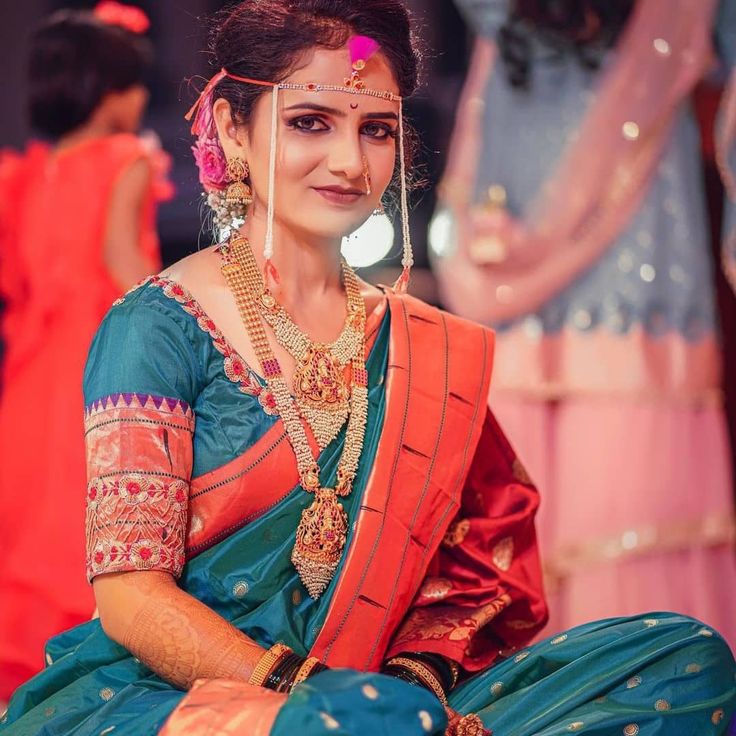 a woman sitting on the ground in a blue and orange sari with gold jewelry