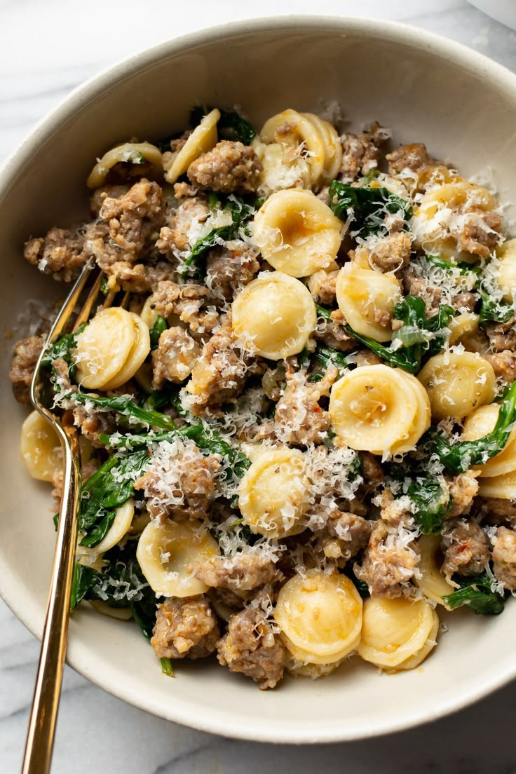 a white bowl filled with pasta and spinach covered in meat, cheese and parmesan