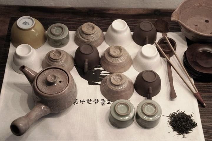 various teapots, cups and spoons are arranged on a white towel with writing