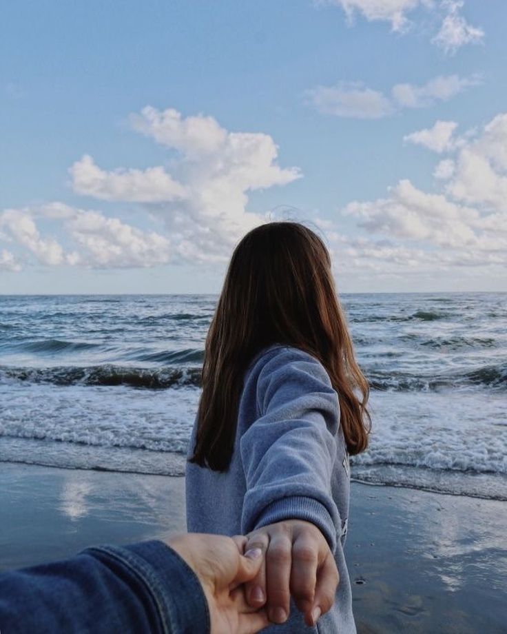 two people holding hands on the beach with waves in the water and clouds in the sky