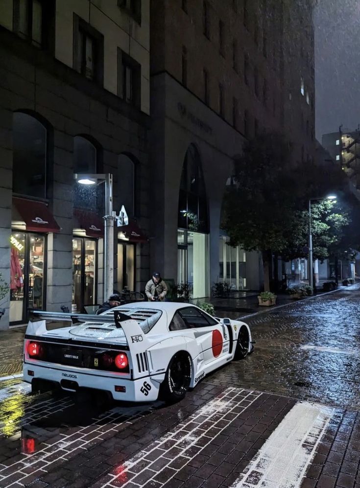 a white sports car parked on the side of a street at night in the rain