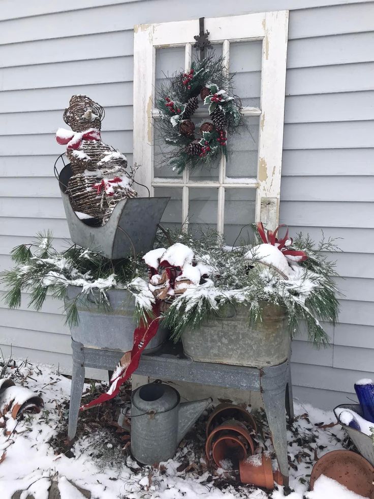 an old window is decorated with christmas wreaths and potted plants in the snow