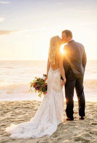 a bride and groom standing on the beach at sunset with the ocean in the background