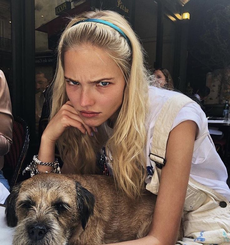 a woman sitting at a table with a dog in front of her and people behind her