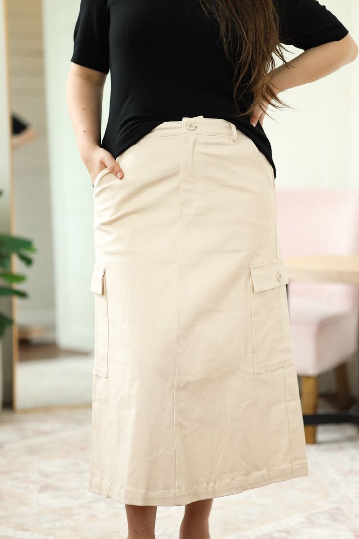 The Cargo Skirt is a must-have item for your style! This skirt has a button and zipper closure with a back elastic waistband. Featuring large cargo pockets on either side, this adorable skirt paired with a sweater or top of your choice will make a great casual outfit! - Button and zipper closure - Back elastic waistband - Belt loops - Hip pockets - Cargo pockets with button and flap closure - 11.5" back split - Maxi length - Material: 97% Cotton | 3% Spandex - Model is 5’6" & wears a M/L. She is Tiered Maxi Skirt With Pockets For Day Out, Spring Utility Beige Cargo Skirt, Utility Style Beige Cargo Skirt For Spring, Utility Beige Cargo Skirt For Spring, Beige Utility Cargo Skirt For Spring, Casual Long Cargo Skirt With Side Pockets, Fall Cotton Skirt With Cargo Pockets, Casual Tiered Skirt With Button Closure, Tiered Skirt Bottoms With Pockets For Day Out