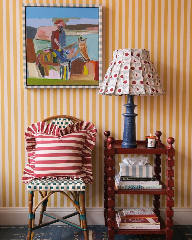 a chair and lamp in front of a painting on the wall next to a table with books