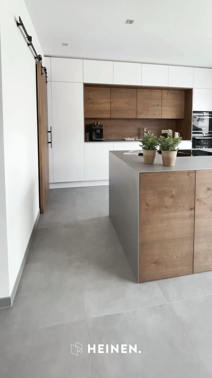 a modern kitchen with an island counter top and wooden cabinetry, along with potted plants