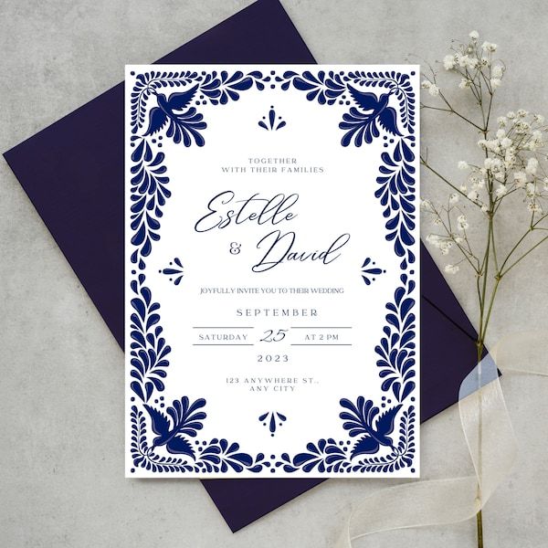 a blue and white wedding card on top of a table next to a bouquet of flowers