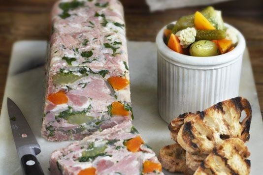 a platter with meat, vegetables and crackers next to a bowl of pickles