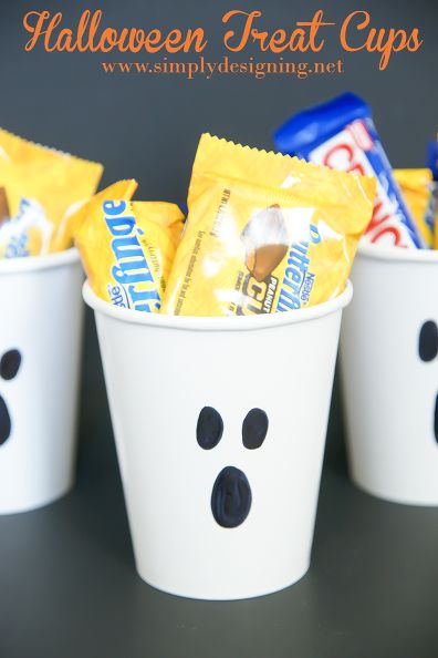 halloween treat cups with candy in them and ghost faces painted on the side, sitting next to each other