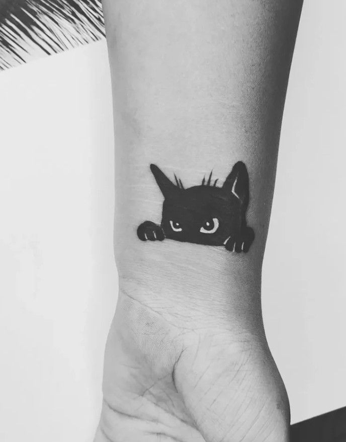 a small black cat tattoo on the wrist