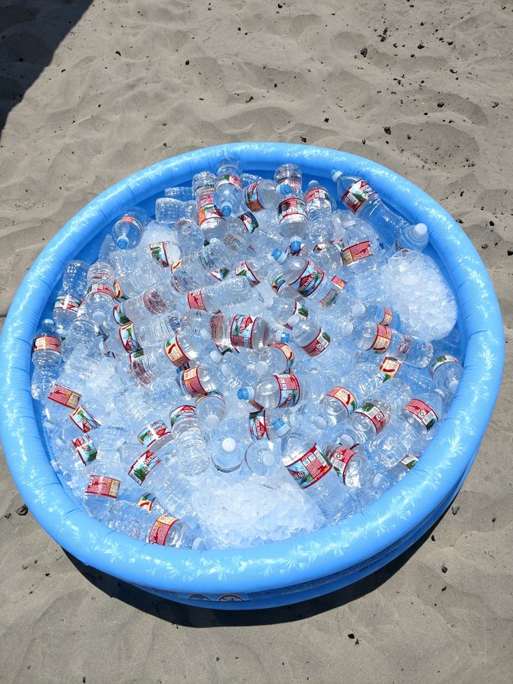 an inflatable pool filled with lots of water and plastic cups on the beach