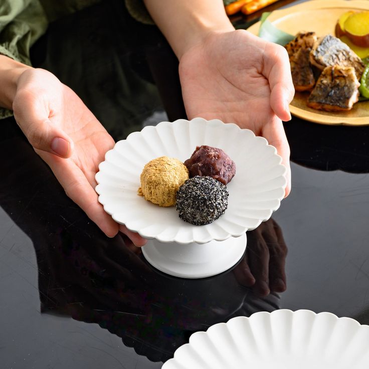 a person holding a paper plate with three different desserts on it and plates in the background