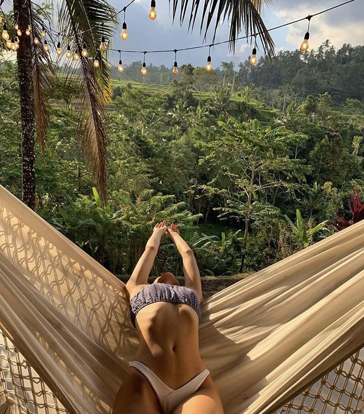 a woman laying in a hammock on top of a lush green forest covered hillside