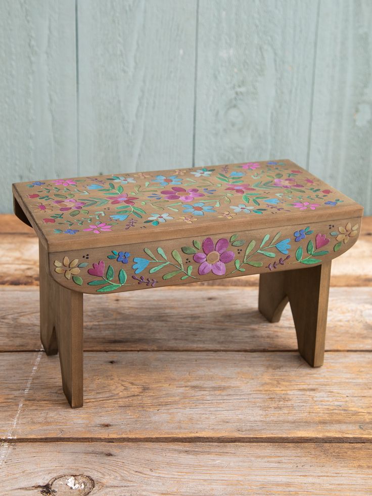 a small wooden bench with flowers painted on the top and bottom, sitting on a wood floor