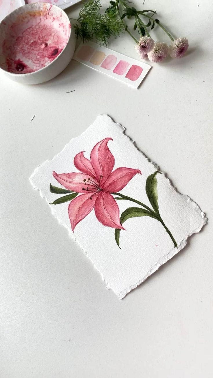 a pink flower painted on a piece of paper next to a bowl with flowers in it