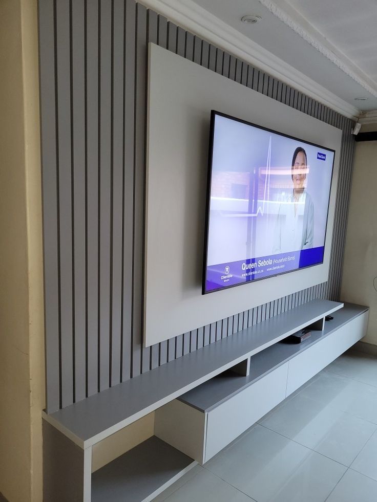 a flat screen tv mounted to the side of a wall next to a white shelf