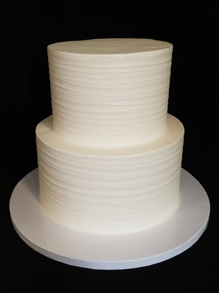 a three tiered white cake sitting on top of a white plate with black background