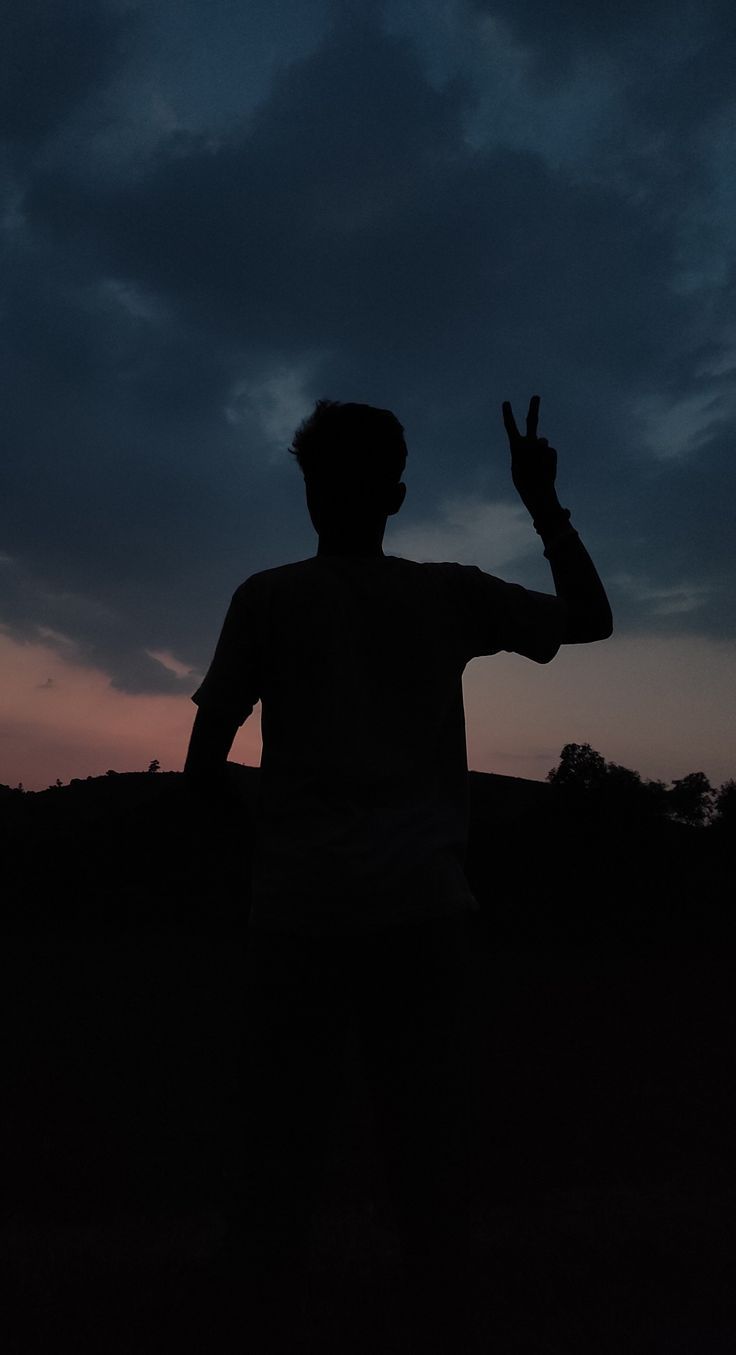 a man standing in the dark holding his hand up to the sky with one hand