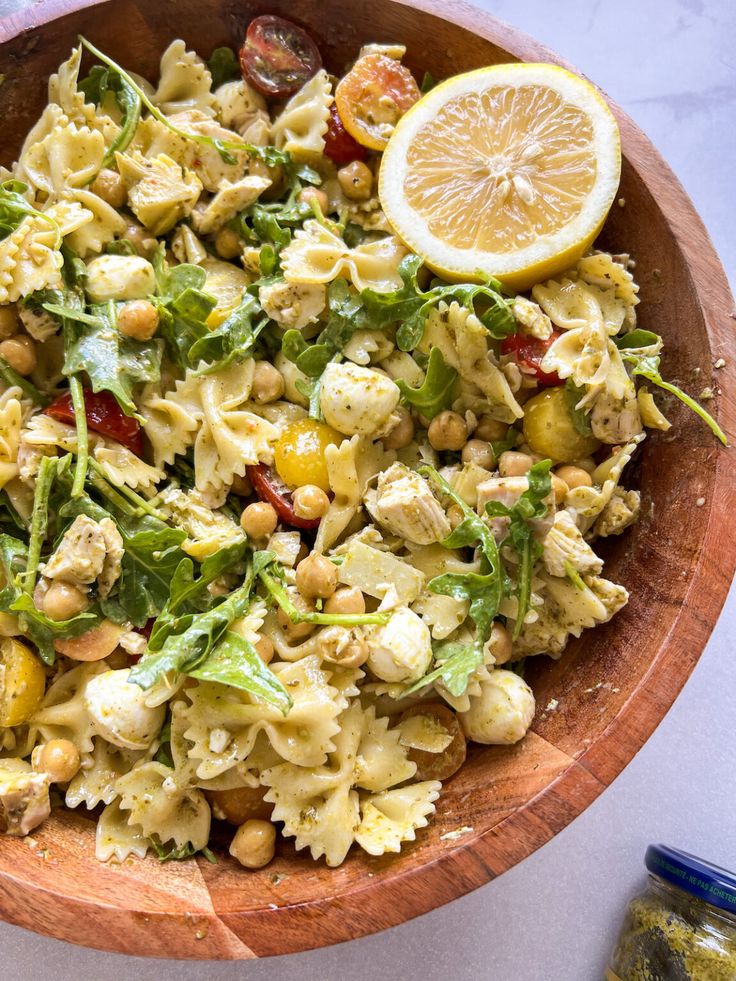 a wooden bowl filled with pasta salad and garnished with lemon wedges on the side