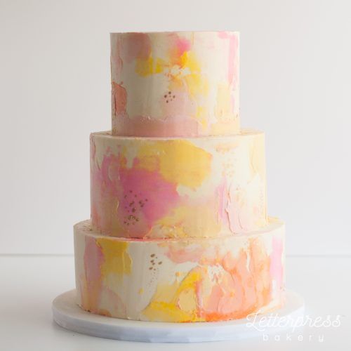 a three tiered cake with pink, yellow and white paint splattered on it