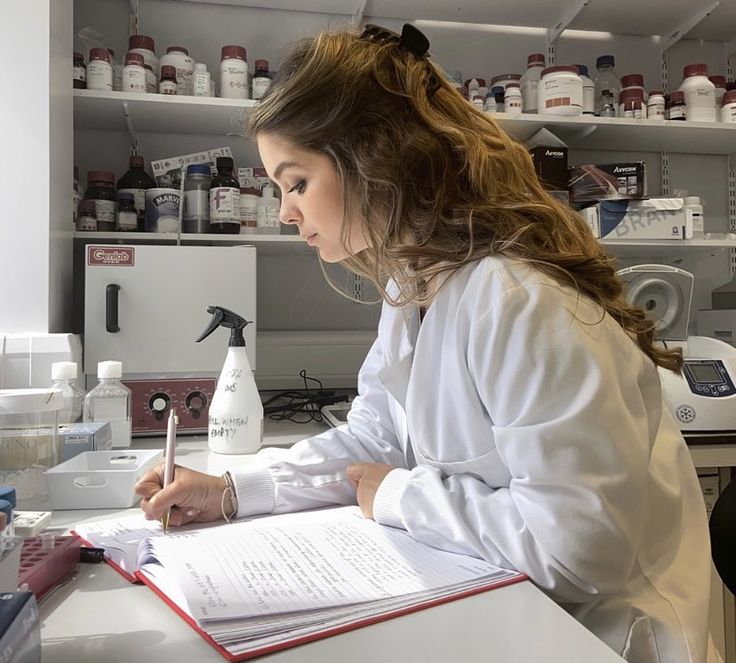 a woman in white lab coat writing on paper