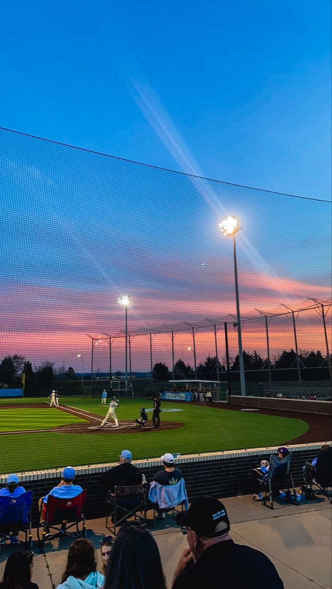 people sitting in chairs watching a baseball game at sunset with the sun setting behind them