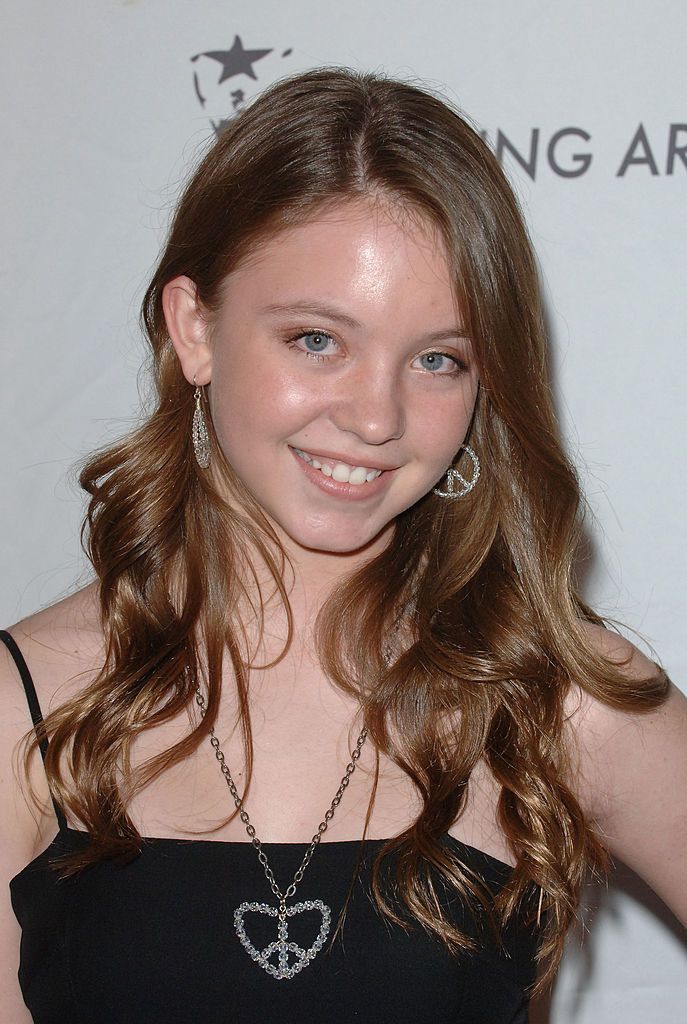 a girl with long brown hair and blue eyes smiles at the camera in front of a white background