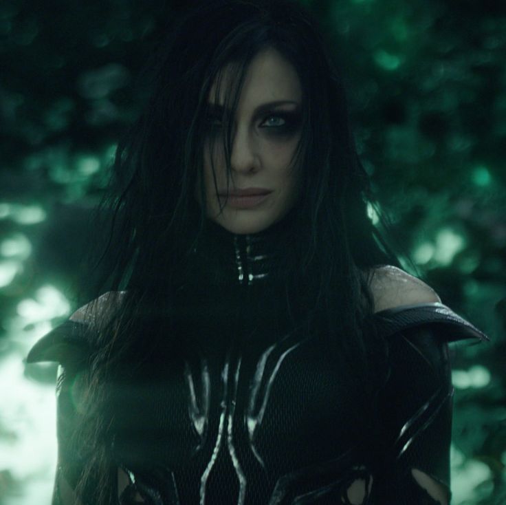 a woman with black hair and leather outfit standing in front of trees