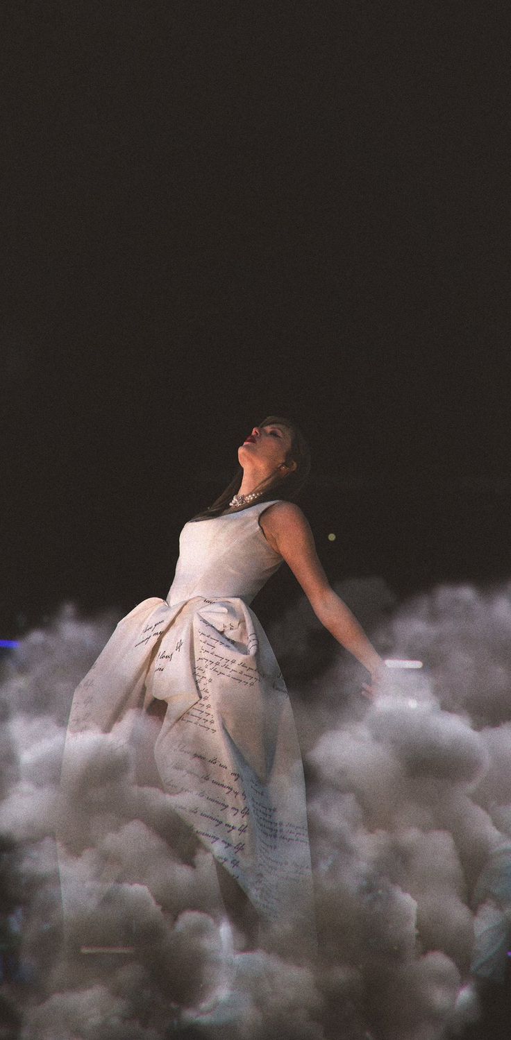 a woman in a white dress standing on top of a pile of clouds with her eyes closed