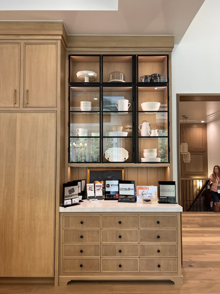 a kitchen with wooden cabinets and white dishes on the counter top, while people are walking in the background