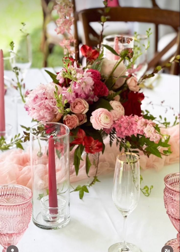 the table is set with pink and red flowers in vases, candles, and glasses